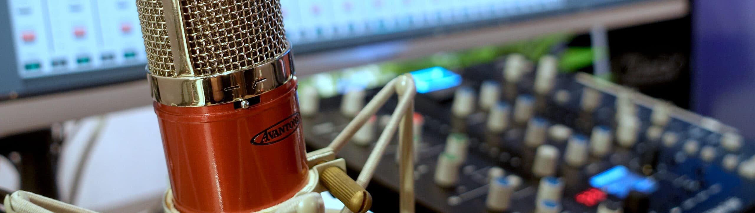 Panoramic close-up of a red Avantone tube microphone in its shockmount, the desk out of focus behind it
